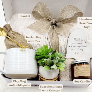 May include: A gift box filled with a white blanket, a burlap bag with tea, a white clay mug with a gold spoon, a succulent plant, a soy candle, and a heart-shaped wooden sign that says "Thank you for being such an important piece of my Life!"