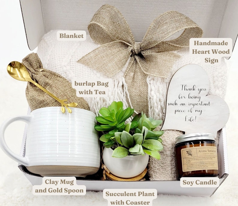 May include: A gift box filled with a white blanket, a burlap bag with tea, a white clay mug with a gold spoon, a succulent plant, a soy candle, and a heart-shaped wooden sign that says "Thank you for being such an important piece of my Life!"
