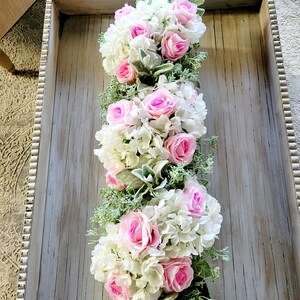 May include: A long, rectangular tray with a whitewashed wood finish and a beaded edge. The tray is filled with a floral arrangement of pink roses and white hydrangeas with green foliage.