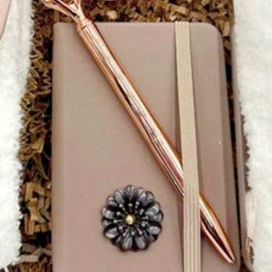 May include: A small brown leather journal with a rose gold pen and a decorative flower embellishment.