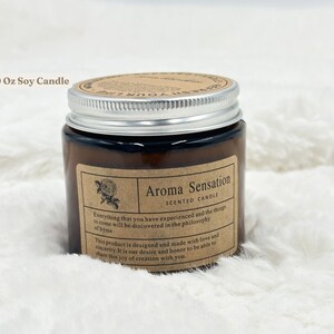 May include: Aroma Sensation scented soy candle in a brown glass jar with a silver lid. The label includes a rose illustration and text that reads "Everything that you have experienced and the things to come will be discovered in the philosophy of byme."