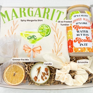May include: A gift box filled with margarita-themed items, including a white t-shirt with the text "MARGARITA Spicy Margarita Shirt", a 16 oz frosted tumbler, a candle, a scrunchie, and a simmer pot mix. The tumbler has a sticker with the text "IT'S CALLED SUMMER WATER IT'S LIKE NORMAL WATER BUT HAS ALCOHOL IN IT".