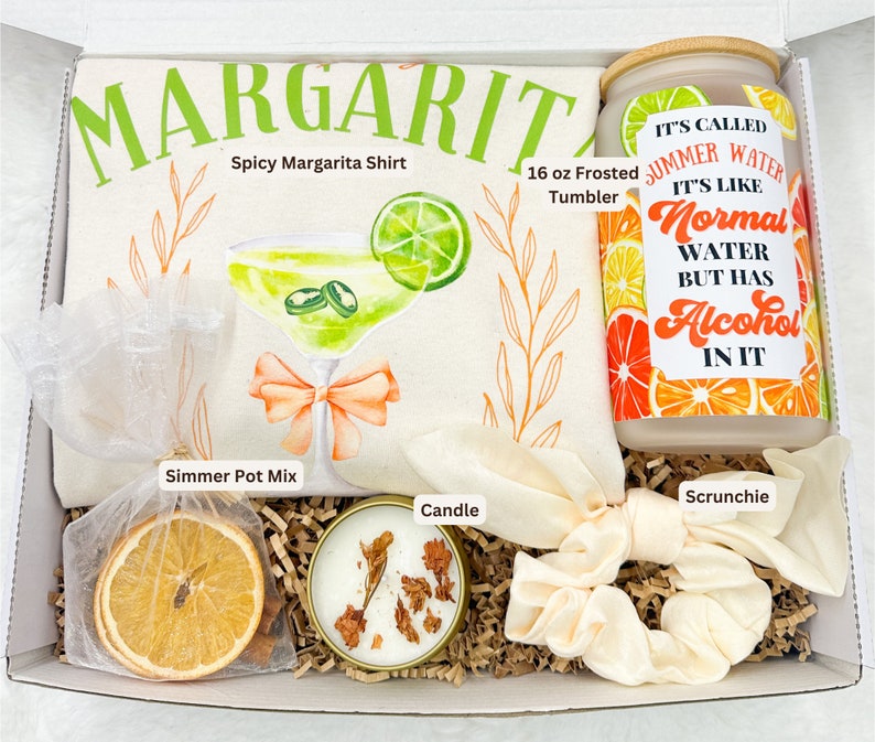 May include: A gift box filled with margarita-themed items, including a white t-shirt with the text "MARGARITA Spicy Margarita Shirt", a 16 oz frosted tumbler, a candle, a scrunchie, and a simmer pot mix. The tumbler has a sticker with the text "IT'S CALLED SUMMER WATER IT'S LIKE NORMAL WATER BUT HAS ALCOHOL IN IT".