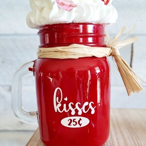 May include: Red glass jar with a white handle, filled with white whipped cream and red cherries. The jar has a white label that says "kisses 25&cent;".