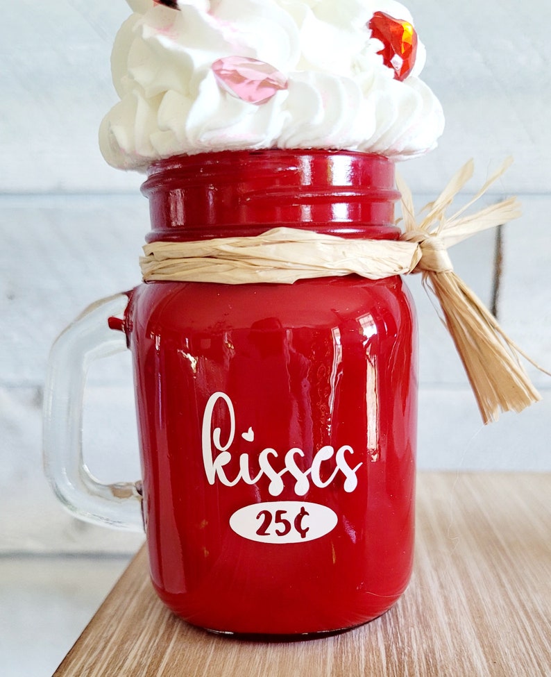 May include: Red glass jar with a white handle, filled with white whipped cream and red cherries. The jar has a white label that says "kisses 25&cent;".