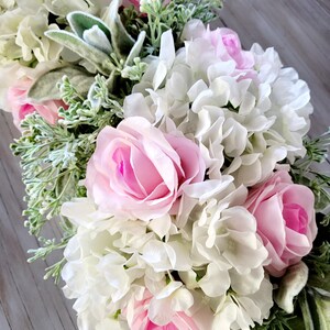 May include: A floral arrangement featuring pink roses and white hydrangeas with green foliage.