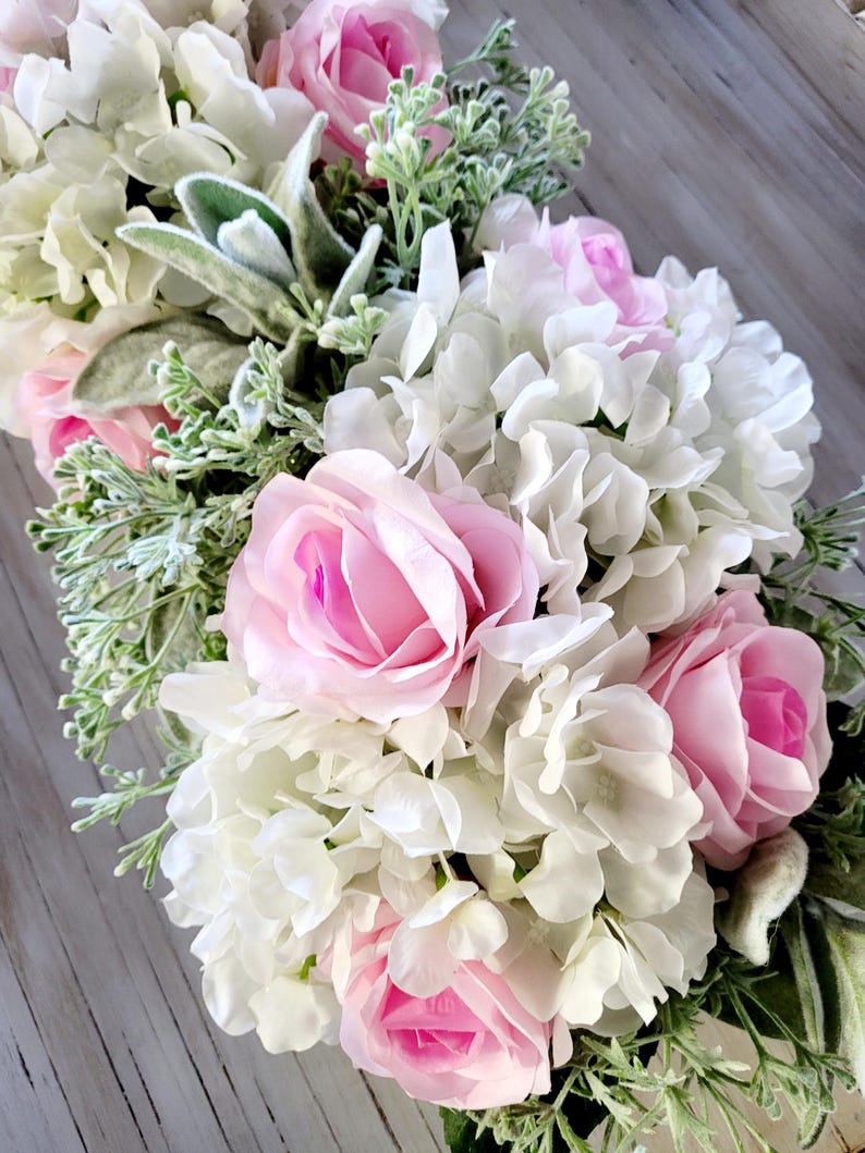 May include: A floral arrangement featuring pink roses and white hydrangeas with green foliage.