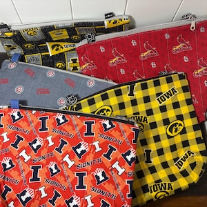 Bolsa grande acolchada con cremallera y forro. Surtido de artículos deportivos. Iowa Hawkeyes. Illinois Illini. Chicago Cubs. St. Louis Cardinals.