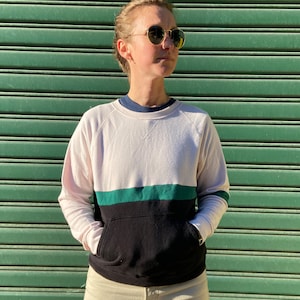 May include: A white, black, and green striped sweatshirt with a kangaroo pocket. The sweatshirt has a relaxed fit and long sleeves.