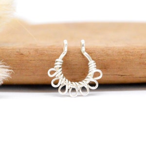 Puede incluir: Anillo de nariz de plata con un delicado diseño de bucles. El anillo está hecho de alambre y tiene una forma circular.