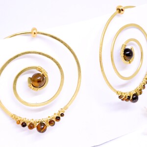 May include: Gold-toned spiral earrings with a central brown gemstone and smaller brown gemstones along the bottom curve. The earrings have a unique, artistic design, perfect for adding a touch of bohemian flair.
