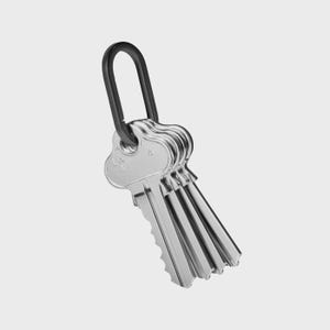 May include: A set of silver keys attached to a black key ring. The keys have a ridged edge and are hanging against a white background. The keys are made of metal and have the letters "LW" and the number "4" on them.