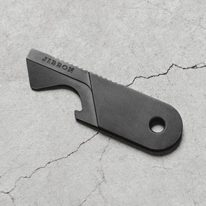 May include: A black metal multi-tool with a bottle opener, a serrated edge, and a hole for attaching a keychain. The tool is engraved with the word "JIRIBON".