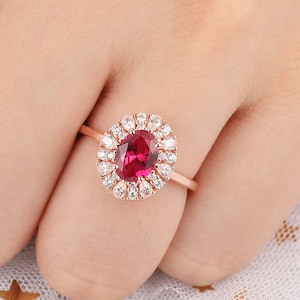 May include: A rose gold ring featuring a large oval ruby surrounded by a halo of smaller diamonds.