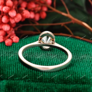 Op de afbeelding: Een gouden verlovingsring met een grote, heldere ovale diamant in een kraalbezetting. De ring ligt op een groene fluwelen ondergrond.