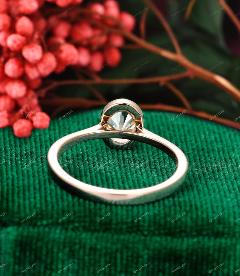 Op de afbeelding: Een gouden verlovingsring met een grote, heldere ovale diamant in een kraalbezetting. De ring ligt op een groene fluwelen ondergrond.