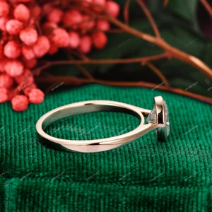 Op de afbeelding: Een gouden verlovingsring met een ronde diamant in een bezel-setting. De ring ligt op een groene fluwelen achtergrond.