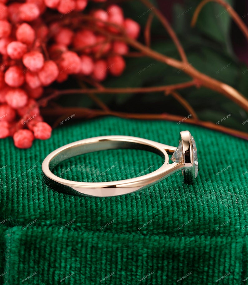 Op de afbeelding: Een gouden verlovingsring met een ronde diamant in een bezel-setting. De ring ligt op een groene fluwelen achtergrond.