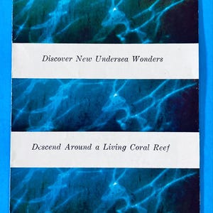 May include: A rectangular brochure for Hawaii's Sea Life Park featuring blue underwater imagery of dolphins and light patterns. The text reads: Hawaii's Sea Life Park, Discover New Undersea Wonders, Descend Around a Living Coral Reef, and Thrill to Amazing Spinning Porpoises.