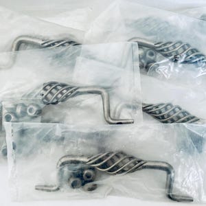 May include: Several silver-toned cabinet pulls with a decorative cage-like design are visible, each individually packaged in clear plastic. The pulls have a curved handle and are accompanied by mounting hardware.