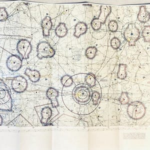 May include: A detailed aviation sectional chart, folded and spread out, displaying a network of lines, circles, and symbols. The chart features various colors, including yellow, blue, and black, against a light background. The chart is designed for navigation and flight planning.