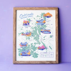 May include: A framed print of a map of Colorado's Alpine Lakes. The map is illustrated with colorful mountains and lakes. The title of the map is "Colorado Alpine Lakes".