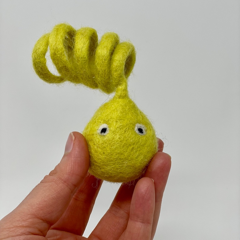 May include: A yellow felt toy with curly yellow felt hair and two white eyes.