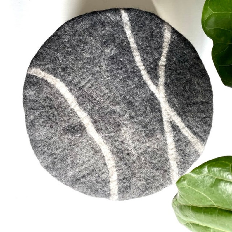 May include: A round gray felt cushion with white abstract lines. The cushion is perfect for adding a touch of modern style to any room.