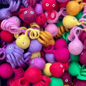 May include: A collection of colourful felt octopus toys in various shades of purple, pink, red, yellow, orange, and green. The octopus toys are made of soft, fuzzy felt and have large, round eyes.