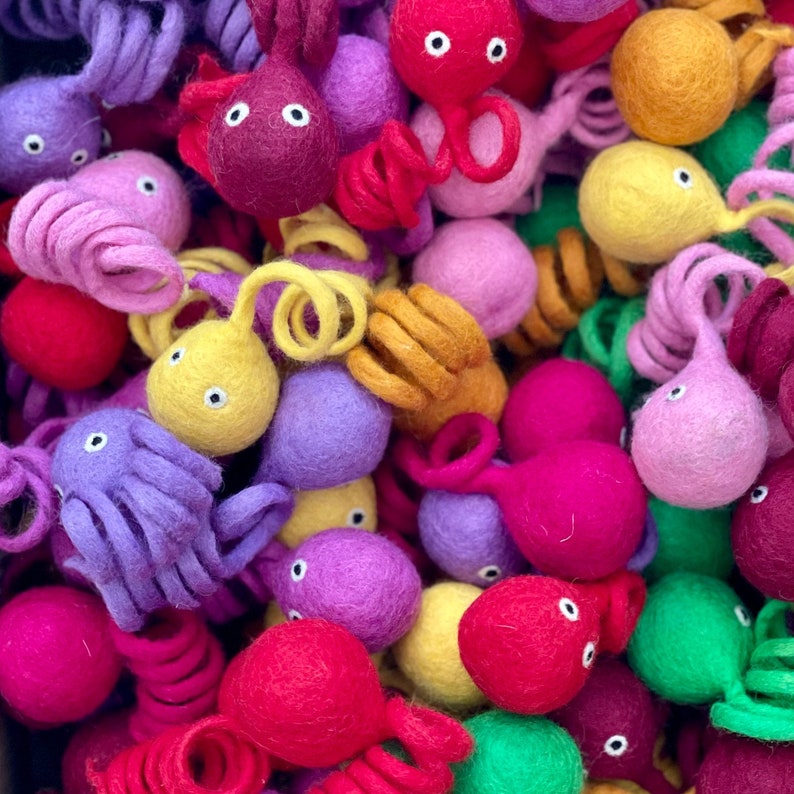May include: A collection of colourful felt octopus toys in various shades of purple, pink, red, yellow, orange, and green. The octopus toys are made of soft, fuzzy felt and have large, round eyes.