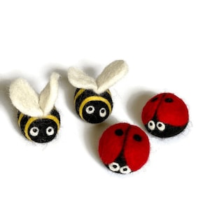May include: Handmade felted bee and ladybug figurines. The bees have black bodies with yellow stripes and white wings. The ladybugs are red with black spots. Each figurine has white eyes.