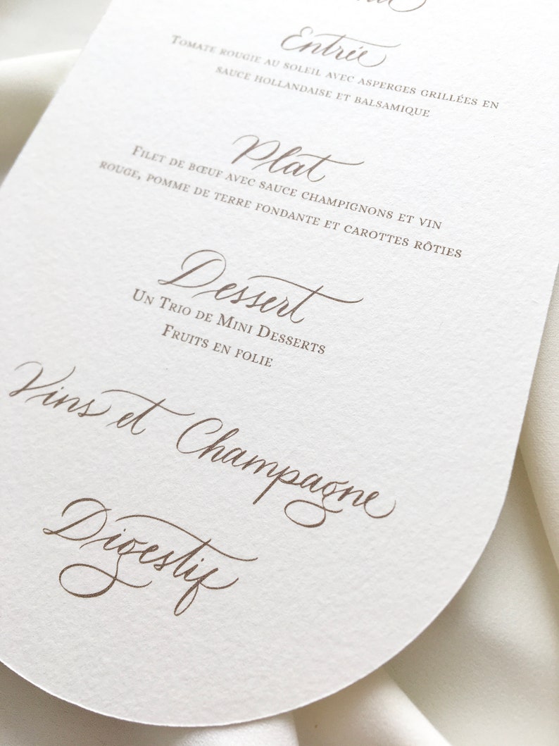May include: A white, round menu card with a brown, handwritten menu. The menu includes the following sections: Entree, Plat, Dessert, Vins et Champagne, and Digestif.