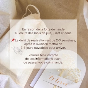 K&ouml;nnte beinhalten: Ein wei&szlig;er Musselinbeutel mit einer handgeschriebenen Notiz, die lautet: "En raison de la forte demande au cours des mois de juin, juillet et ao&ucirc;t. Le d&eacute;lai de r&eacute;alisation est de 2-3 semaines, apr&egrave;s la livraison mettra de 3-5 jours ouvrables pour arriver. Veuillez tenir compte de ces informations avant de passer votre commande. Merci." Die Notiz befindet sich auf einer wei&szlig;en Karte mit einem kleinen Zweig wei&szlig;er Blumen.
