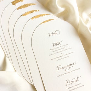 May include: A stack of white, oval-shaped cards with gold accents. The cards feature a French menu with the headings "Menu", "Plat", "Fromages", and "Dessert".