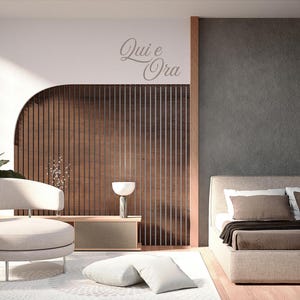 May include: A modern bedroom interior with a neutral color palette. Features a beige upholstered bed, a rounded armchair, and a wooden slatted wall. The text "Qui e Ora" is visible on the wall. The room is decorated with plants and a decorative lamp.
