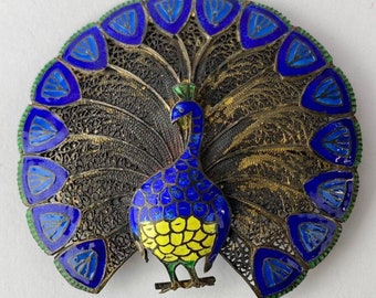 Peut inclure: Une broche en argent et émail représentant un paon avec des accents bleus, verts et jaunes. Les plumes de la queue du paon sont déployées en éventail.