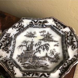 May include: A white octagonal ceramic serving dish with a black and grey design of a Chinese garden scene. The design features a bridge, trees, and buildings.