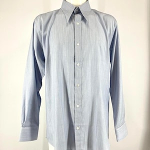 May include: A light blue dress shirt with vertical stripes. The long-sleeved shirt has a pointed collar and button-down front. The cuffs are buttoned. The shirt is displayed on a mannequin.