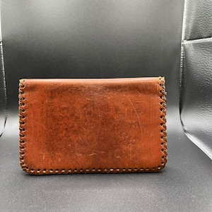 May include: A rectangular, brown leather wallet with visible stitching along the edges. The wallet has a worn appearance, suggesting it is well-used. The leather has a slightly distressed look.