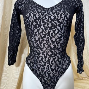 Puede incluir: Body negro transparente con estampado floral. El body tiene mangas largas y cuello en V.