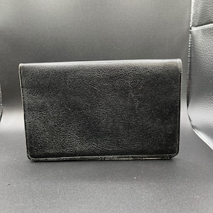 May include: A closed, black leather wallet with a textured finish. The rectangular wallet has visible stitching around the edges. The background is a dark grey.