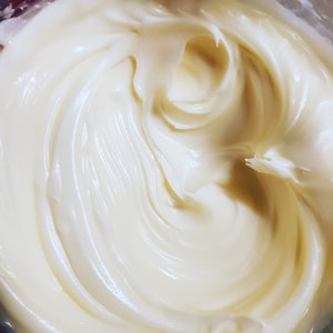 May include: Close-up of a smooth, white, creamy substance in a container. The substance is swirled and has a glossy finish.