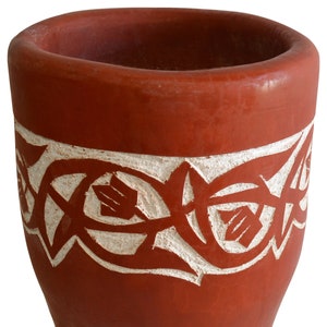 May include: A terracotta planter with a white carved design around the top. The planter is a cylindrical shape with a rounded bottom.