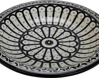 May include: A large, round, white ceramic serving dish with a black and white geometric design. The dish has a raised rim and a scalloped edge.