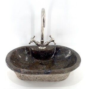 May include: An oval-shaped, dark brown stone sink with a white rim. The sink has a textured surface and a single faucet with two handles.