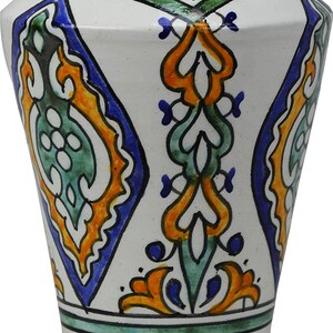 Peut inclure: Un vase en céramique blanche avec un motif géométrique bleu, vert et orange. Le vase a une large ouverture et une base étroite.