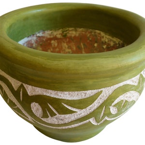 May include: A green ceramic planter with a white carved design. The planter has a wide, round opening and a slightly rounded bottom.