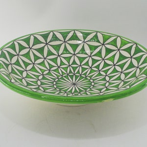 May include: Oval ceramic serving bowl with a green rim and a white interior. The bowl's interior features a repeating pattern of green and white geometric shapes, outlined in black. The bowl is ideal for serving food.