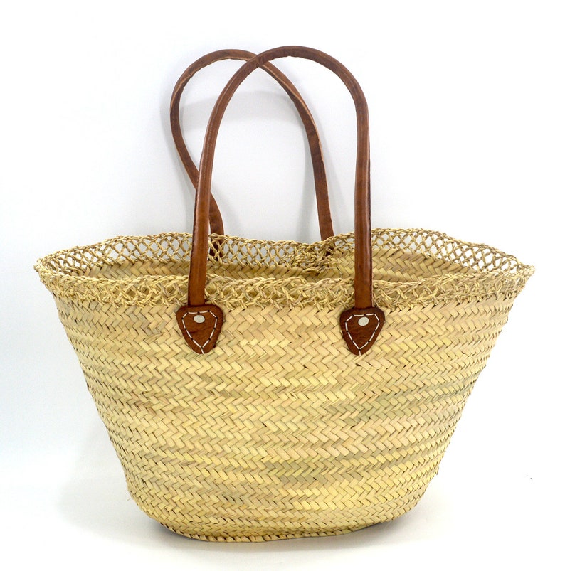 K&ouml;nnte beinhalten: Eine gro&szlig;e, geflochtene Strohtasche mit braunen Ledergriffen und einem geh&auml;kelten Besatz. Die Tasche hat ein Fischgr&auml;tenmuster und ist perfekt zum Tragen von Lebensmitteln oder anderen Gegenst&auml;nden.