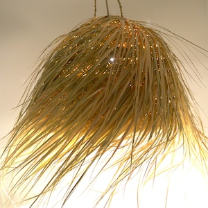 May include: A woven pendant light made of natural materials, resembling a large, fluffy, light brown ball of grass.